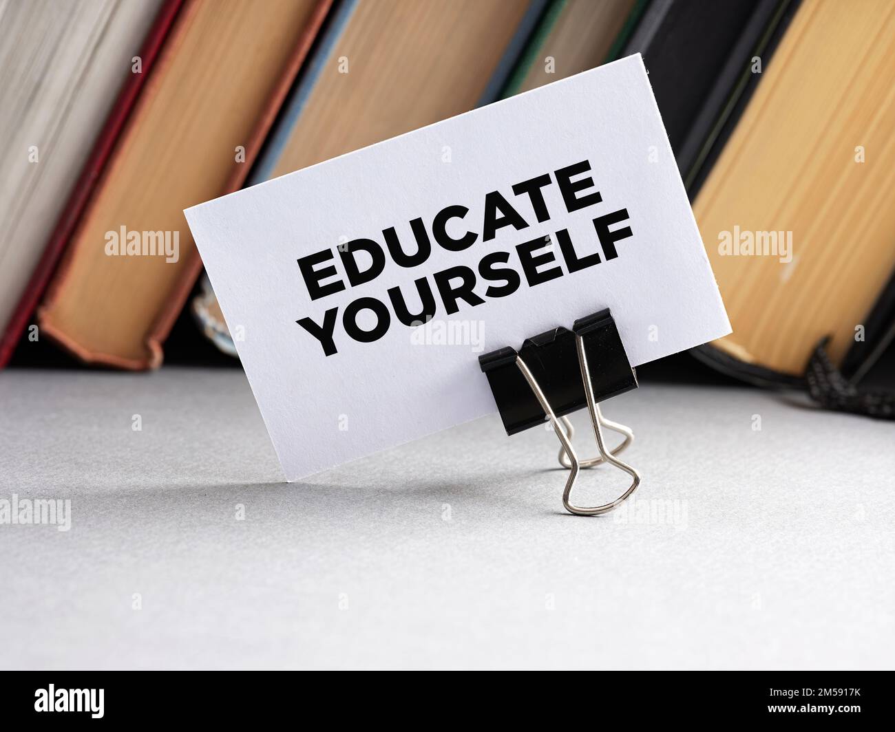 The message educate yourself written on a business card with books background. Self education training guidance or consultancy concept. Stock Photo