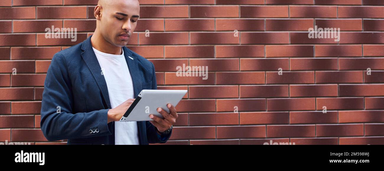Using gadget. Young guy standing on wall browsing internet on digital tablet concentrated Stock Photo