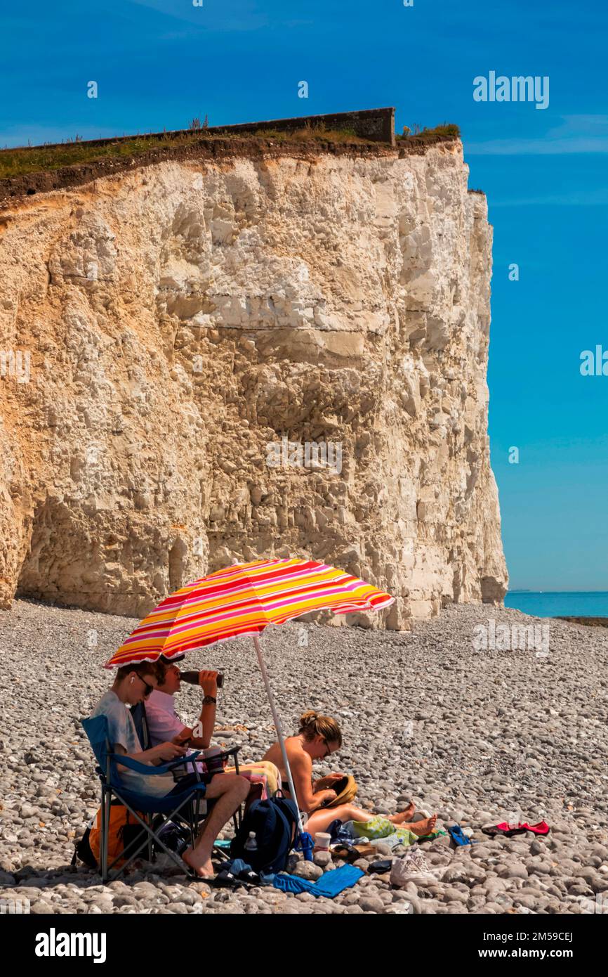 England, East Sussex, Eastbourne, The Seven Sisters Cliffs, The Birling Gap, Family with Colourful Parasol Relaxing on Beach *** Local Caption ***  UK Stock Photo