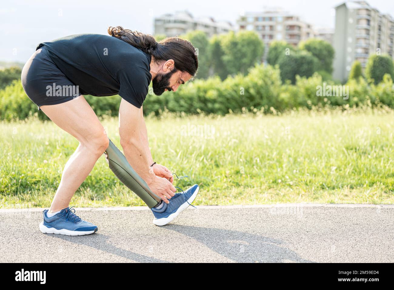 Young man with an artificial prosthesis replacing a leg prepares to train and fastens the straps of the artificial foot shoe, copy space Stock Photo