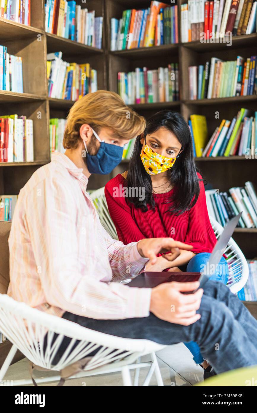 Two young students in a library with protective mask on their face to ...