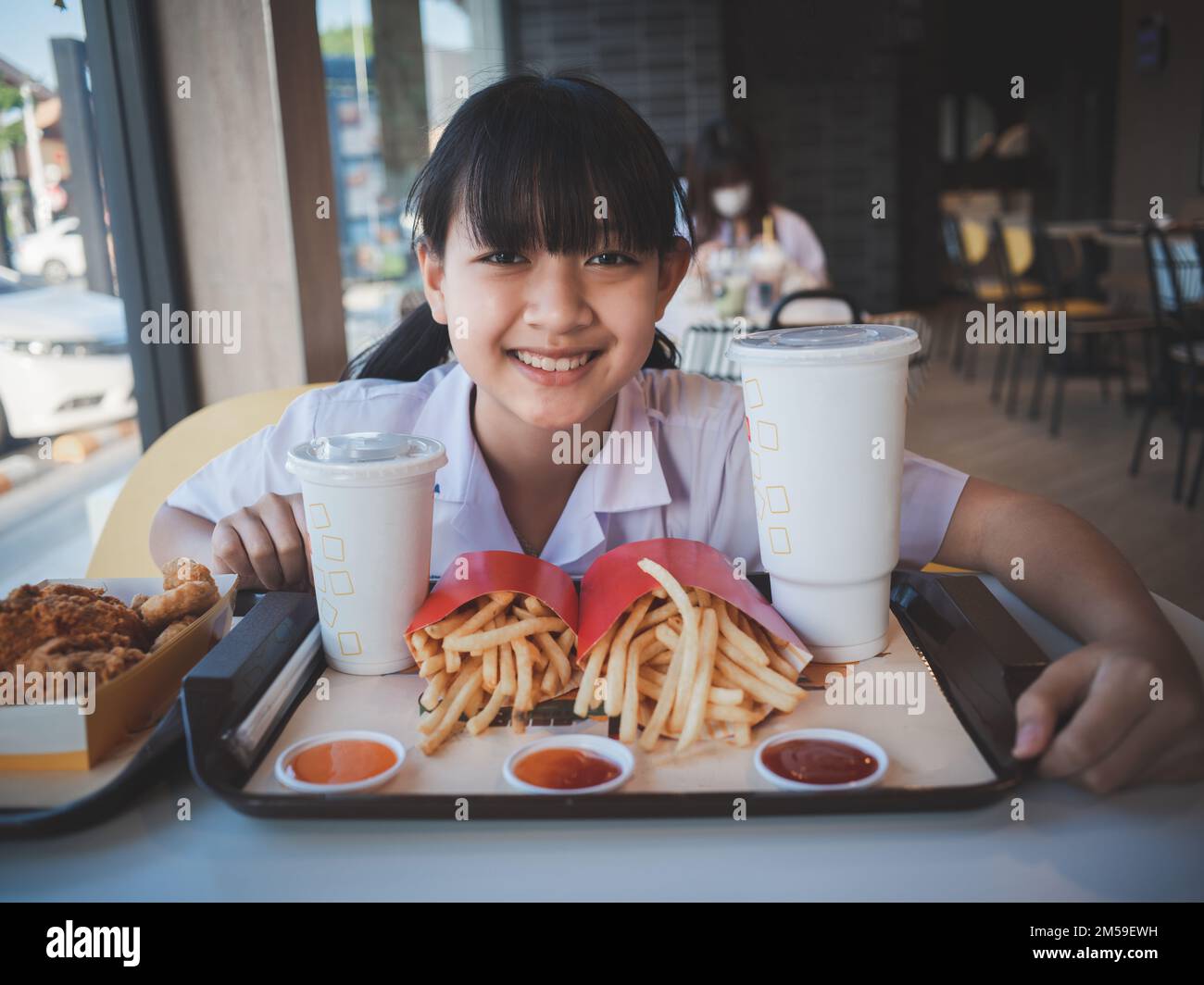 Asian cute girl eating a fast food set with fries , drink and fried chicken in a cafe. Fast food and healthy food for child concept Stock Photo