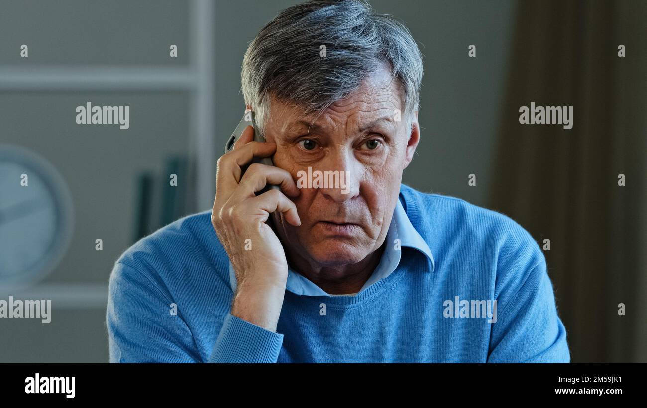 Close-up portrait male sad wrinkled face old caucasian man angry grandpa upset unhappy frustrated senior mature grandpa client talking phone conflict Stock Photo