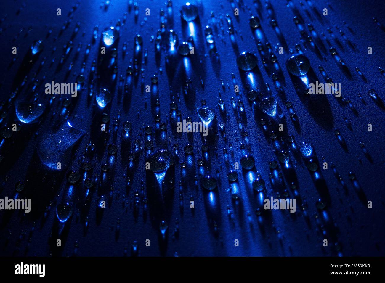 Round drops of water on dark blue background. Through transparent drops of water pass rays of light. View from top. Beautiful back for screensaver. Abstract background.. Stock Photo