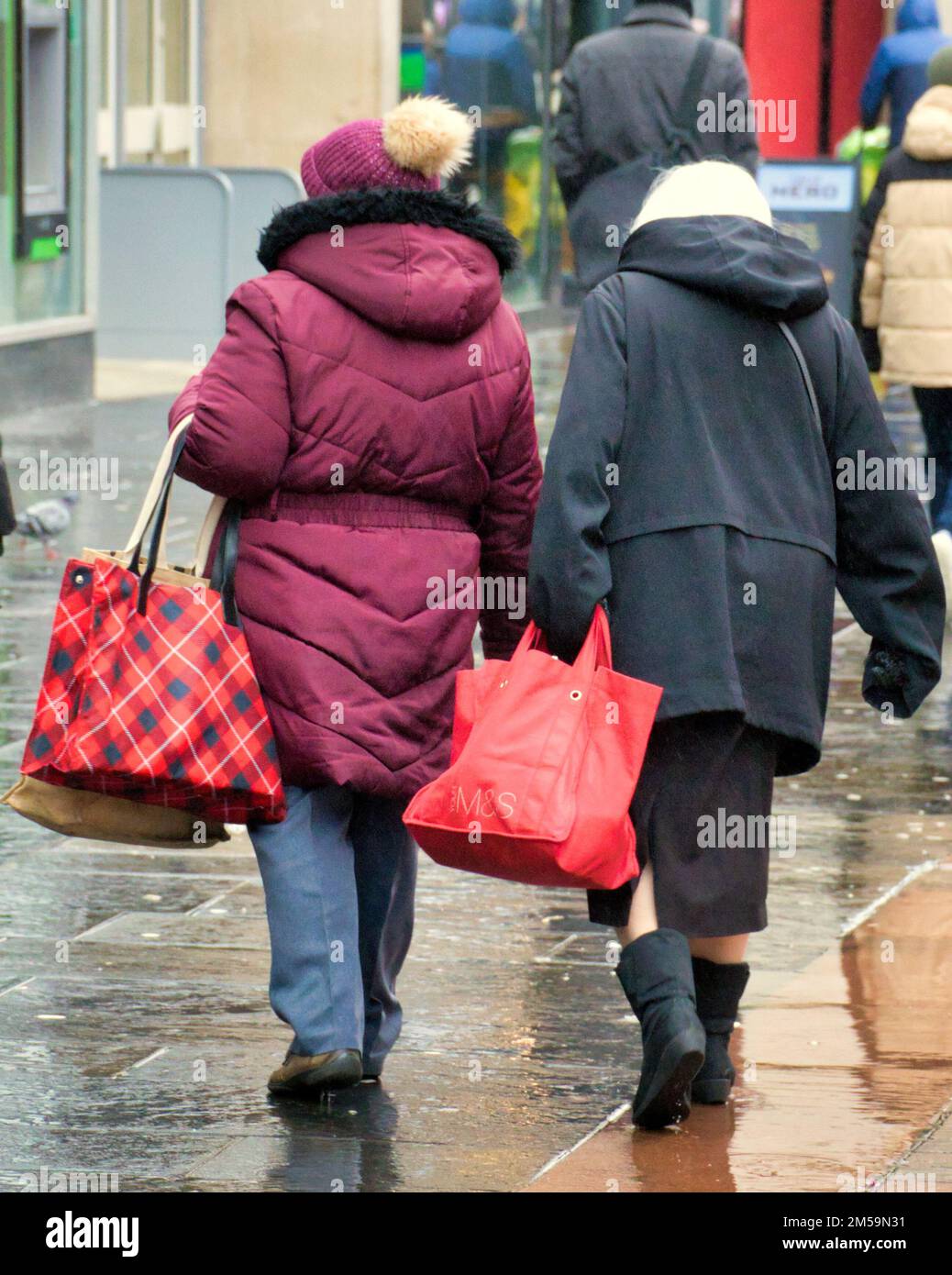 Two women with shopping bags from behind in the cold rain Stock Photo