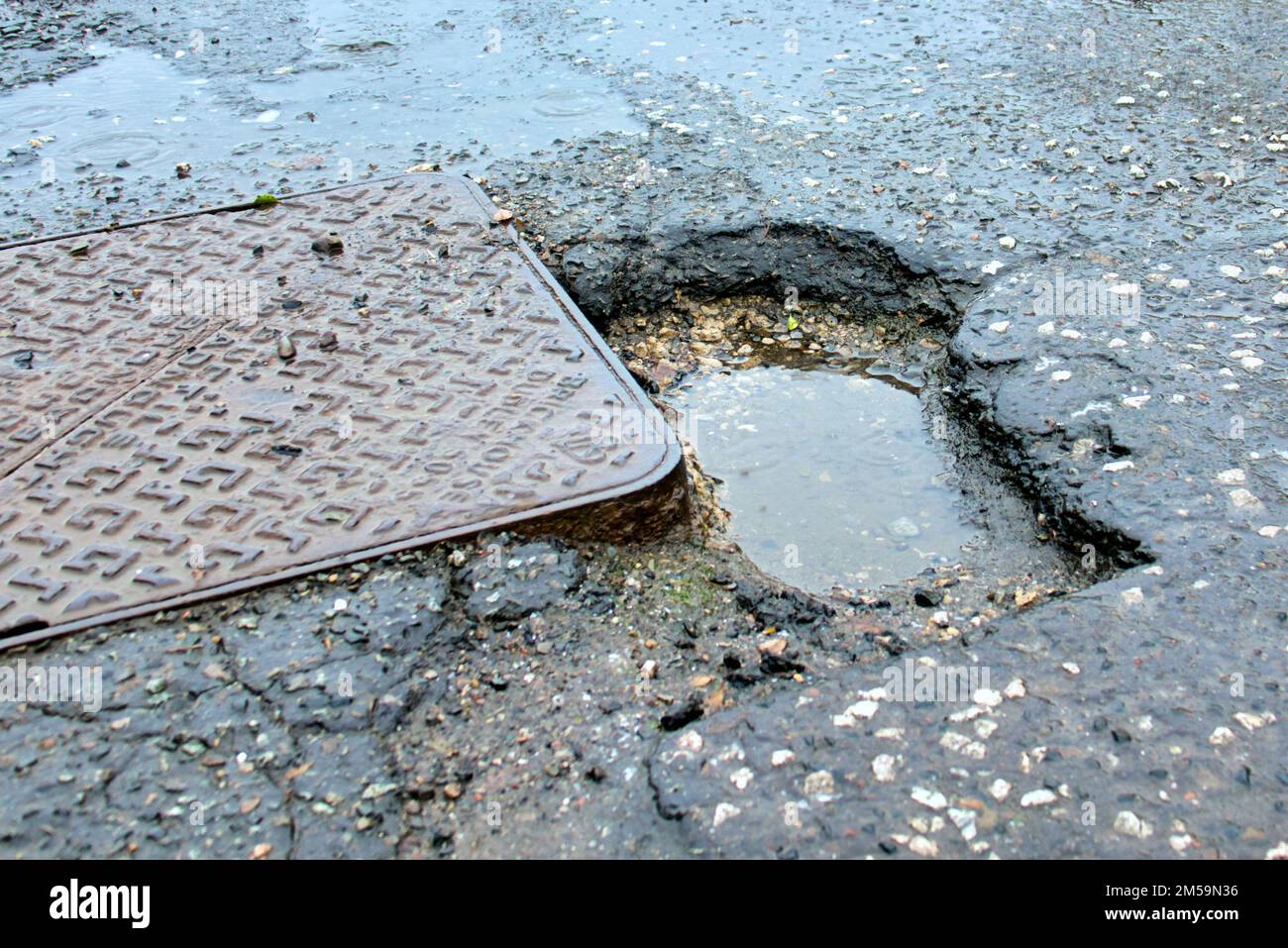 Dangerous pothole in middle of road beside drain cover Stock Photo