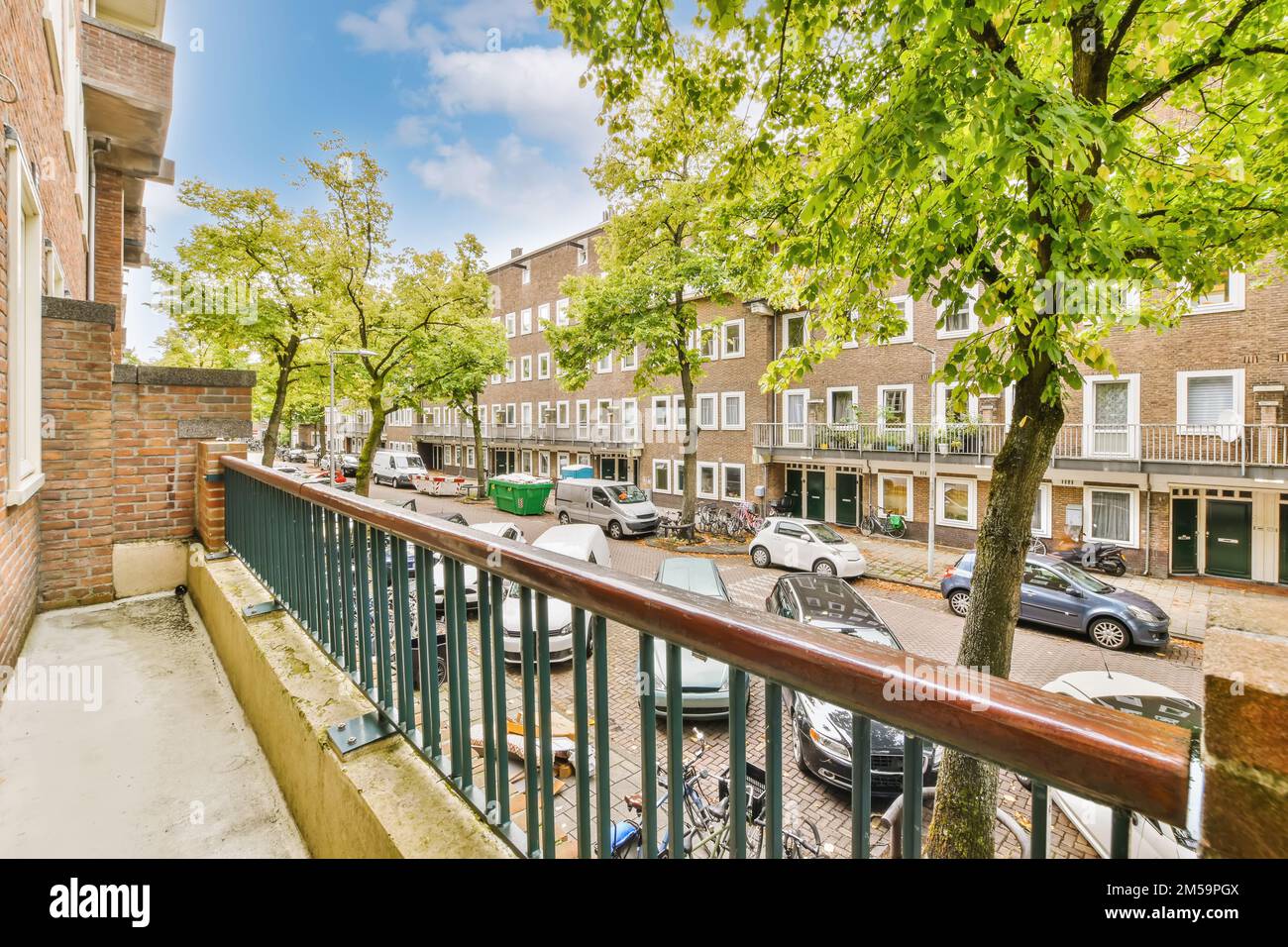 an apartment balcony with cars parked on the street and trees in the ...