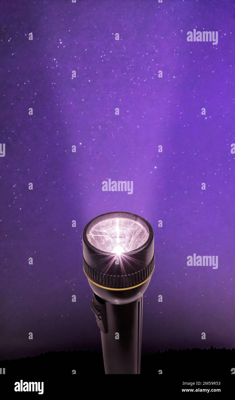 Flashlight sending a beam of light into a starry purple night sky. Stock Photo