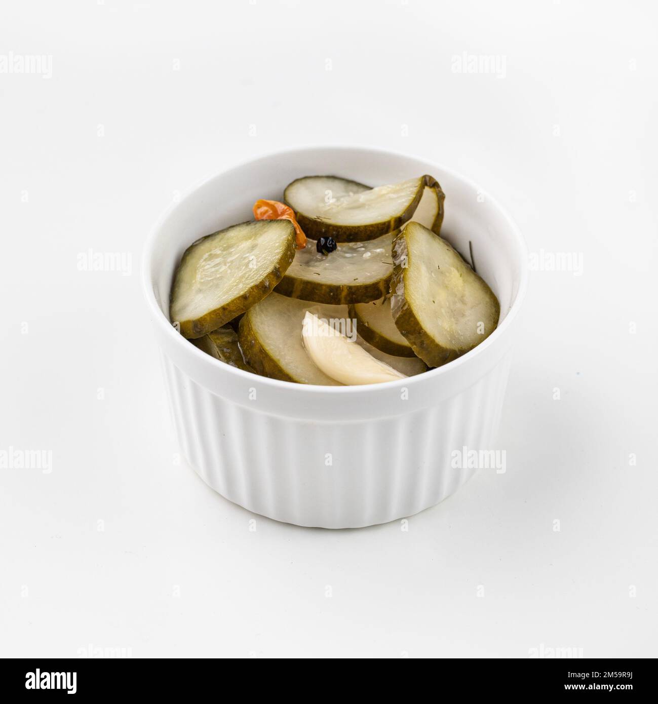 Pickled sliced cucumbers in brine in a bowl on white background. Traditional meat snacks. Healthy fermented food. Stock Photo