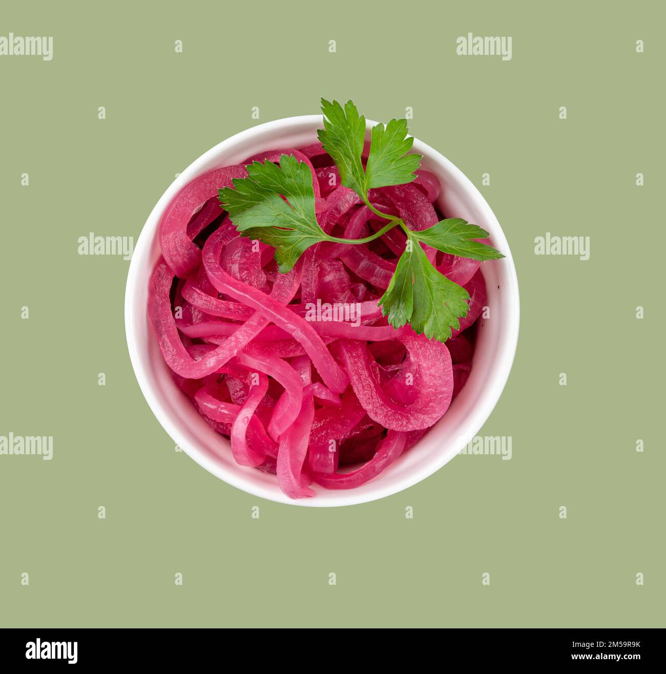 Pickled red onion rings in a white bowl with fresh herbs on green background. Healthy fermented food. Top view. Stock Photo