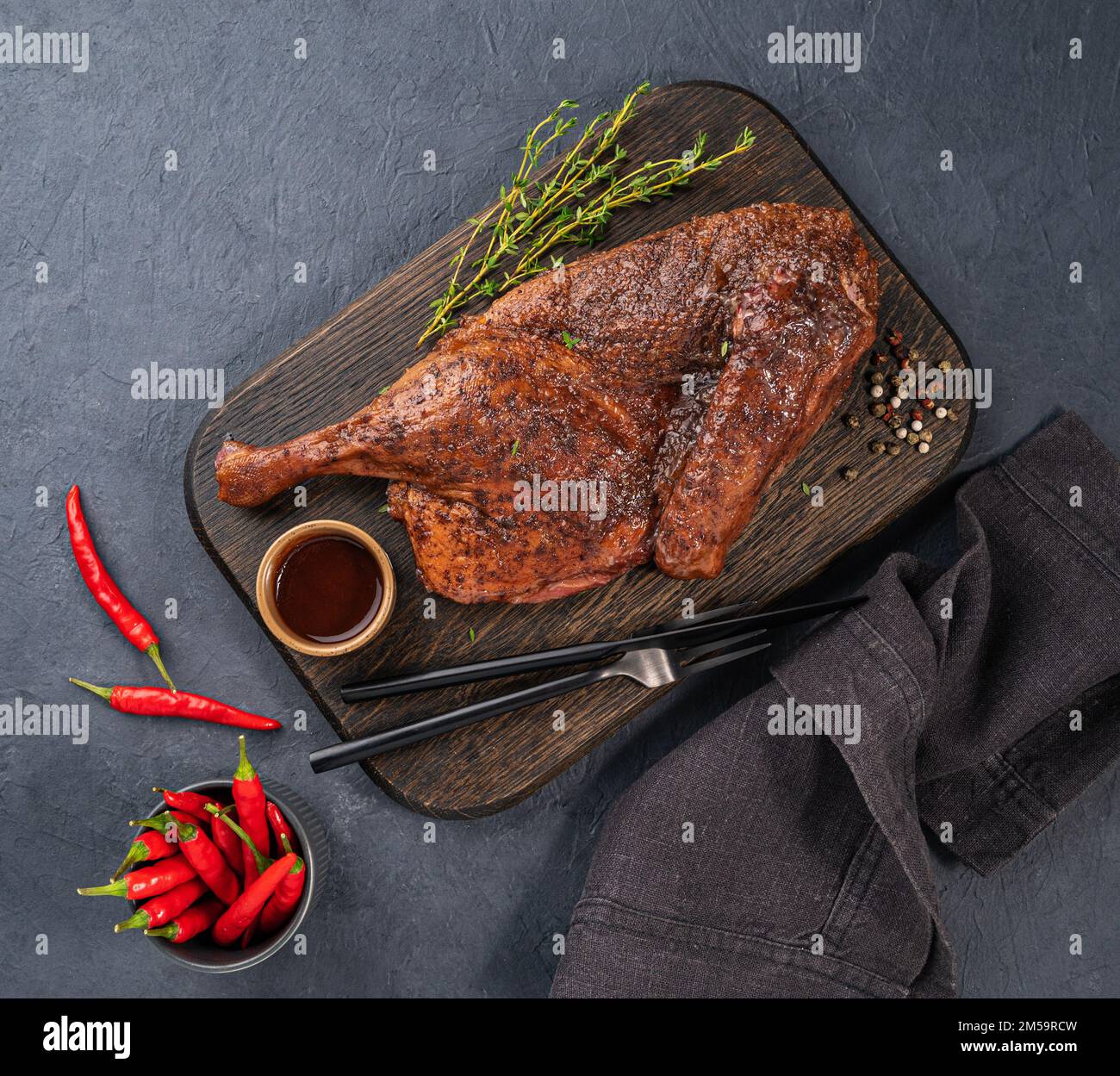 BBQ roast duck or chicken in spices and marinade on a wooden board with fresh spices and chili pepper on dark background. Top view and copy space. Stock Photo