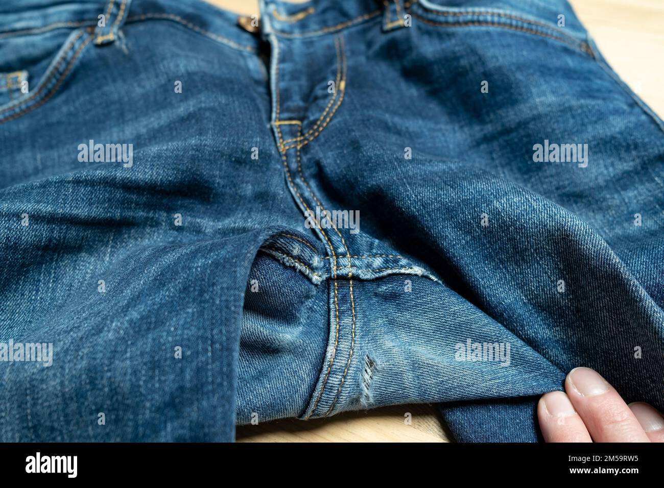 Hole in jeans. Worn, old denim trousers on a wooden table.  Stock Photo