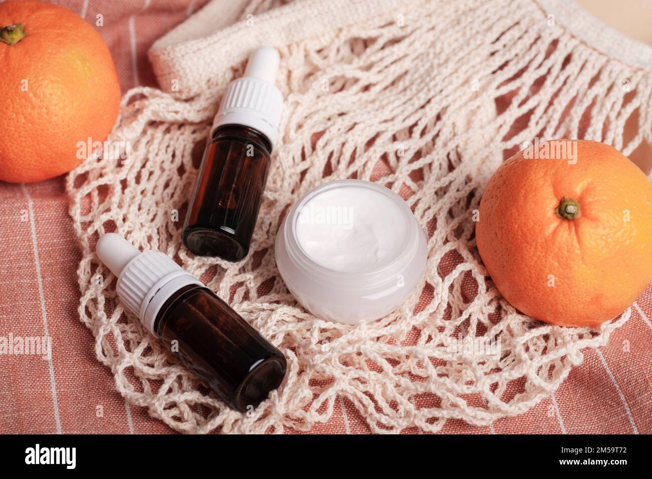 Cream jar and essential oil bottles on the background of cotton mesh bag and tangerines. Organic spa cosmetic beauty product. Zero waste concept. Stock Photo