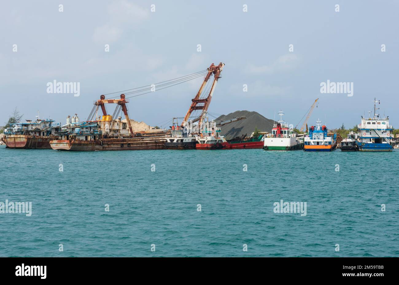 Small cargo ships moored in commercial industrial shipping port on island tropical lagoon Stock Photo