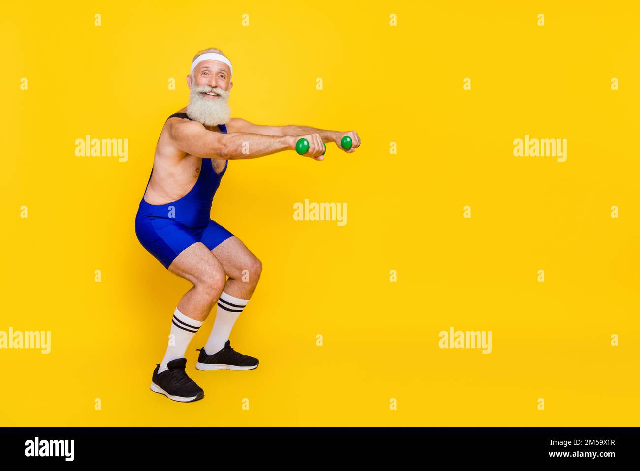 Photo of funky positive retired guy wear blue overall pumping arms sit ups empty space isolated yellow color background Stock Photo