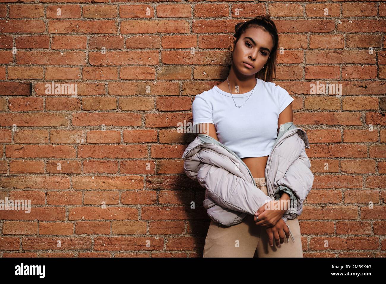 Young woman looking at the camera while posing against a brick wall. Stock Photo