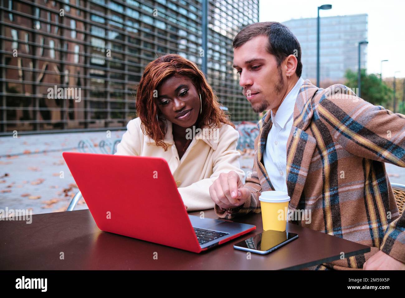 Two business people working together on a laptop while sitting at an outdoor cafe. Stock Photo