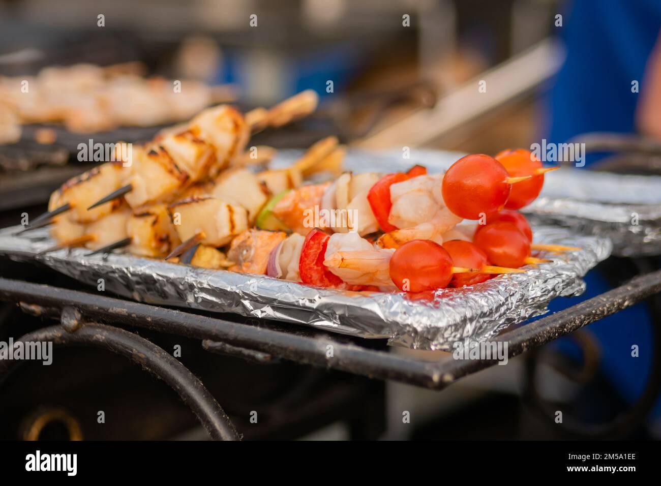 Cooked scallop and shrimp, prawn skewers, cherry tomato on foil - street food Stock Photo