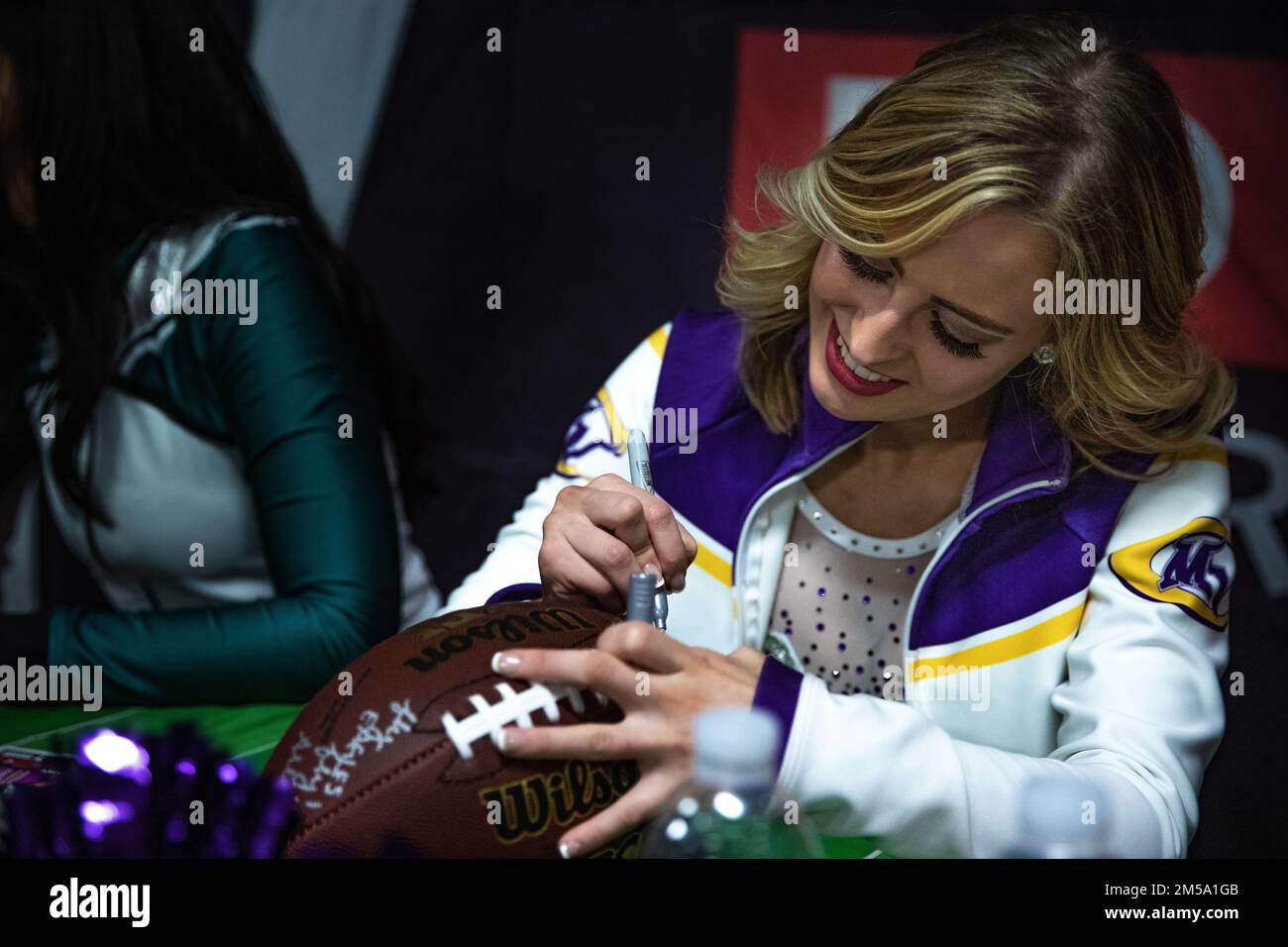 Casey McNally, a cheerleader with the Minnesota Vikings, signs a football picture during a meet and greet event held at Poznan, Poland, Feb. 13, 2022. As part of the event, the Soldiers had the opportunity to take pictures, get autographs, and watch the Super Bowl with the NFL player and cheerleaders. Stock Photo