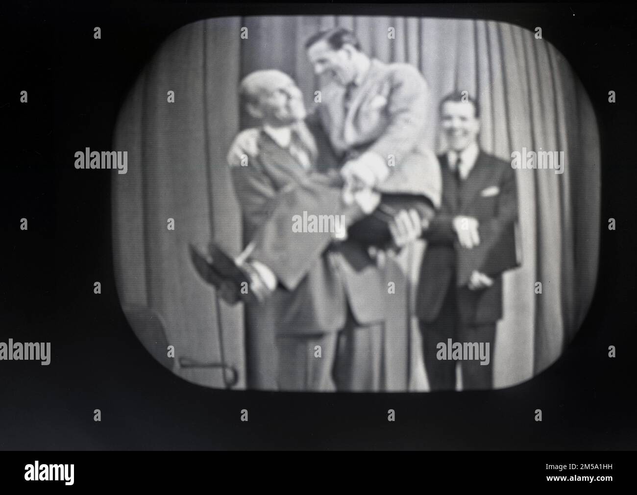 1957, historical, an image from a television broadcast of the British comedic actor, Nornan Wisdom being held up by magician David NIxon on the show, This Is Your Life, presented by Irish broadcaster Eamonn Andrews. This was filmed at the Playhouse Theatre, Manchester. Wisdom was also a subject of This Is Your Life again in 1987. Andrews was the show's host from 1955 to 1964 and again from 1969 to 1987. The British version, first shown in 1955 on the BBC was presented by its American creator Ralph Edwards and its subject was Eamonn Andrews, who would go on to become its much-loved host. Stock Photo