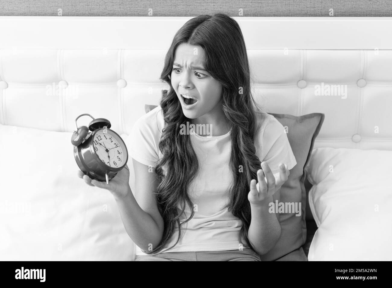 Slept right through the alarm. Girl scream looking at alarm clock. Child in panic sit in bed Stock Photo