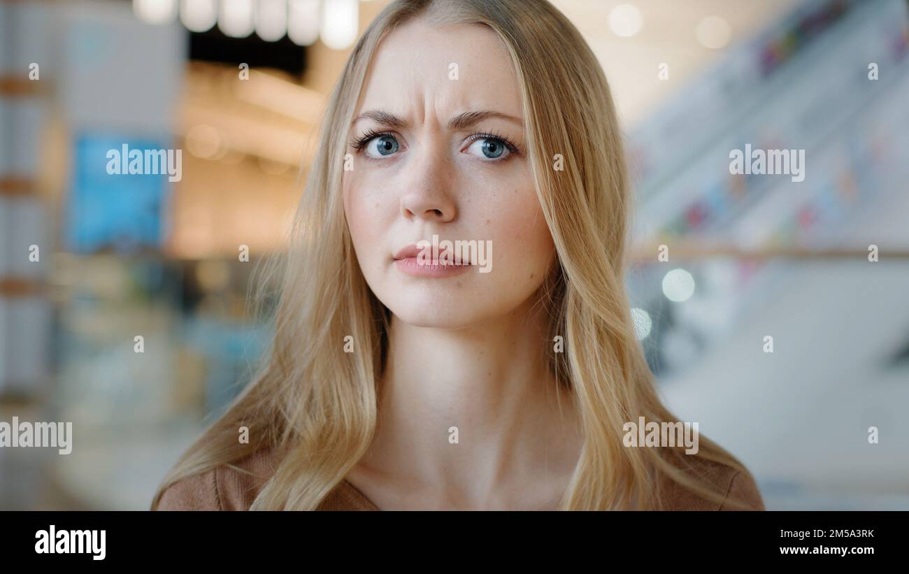 Close-up sad angry serious female face indoors portrait blond 20s girl millennial Caucasian woman lady confused female looking at camera puzzled Stock Photo