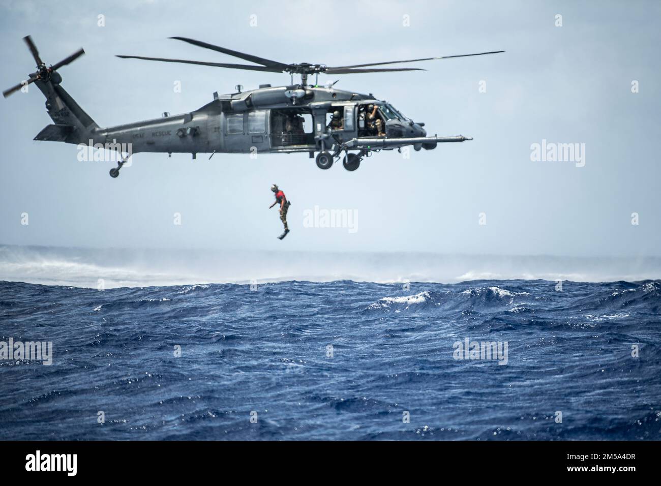A U.S. Air Force pararescueman with the 31st Rescue Squadron jumps out of an HH-60G Pave Hawk from the 33rd Rescue Squadron during exercise Cope North 22 at the Island of Tinian near Andersen Air Force Base, Guam, Feb. 14, 2022. Japanese and U.S. Air Force members trained together in participation of Cope North 2022, multilateral U.S. Pacific Air Forces-sponsored field training exercise conducted annually at Andersen AFB, Guam focused on combat air forces’ large-force employment and humanitarian assistance and disaster relief training to enhance interoperability among U.S., Australian, and Jap Stock Photo