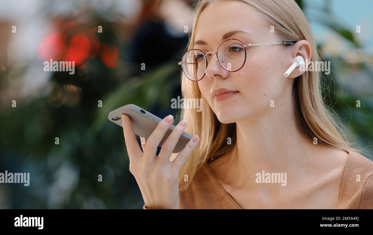 Close up emotional girl use virtual assistant speak in microphone of phone caucasian young lady with glasses talk on speakerphone record audio message Stock Photo