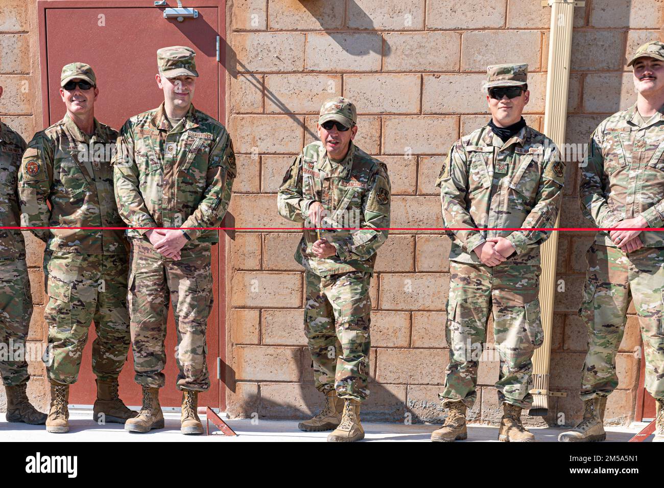 U.S. Air Force Col. John Gustafson, commander of the 386th Expeditionary Mission Support Group, cuts a ribbon to commemorate the finished construction and opening of a new building for the Force Protection Flight at Ali Al Salem Air Base, Kuwait, Feb 14, 2022. This is the first permanent structure on base that coupled U.S. building standards with local standards, using a lot of local material, which decreased cost and construction time. Stock Photo