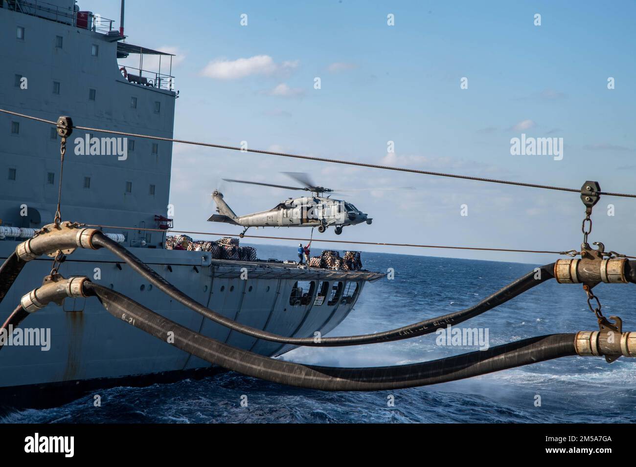 PHILIPPINE SEA (Feb. 15, 2022) An MH-60S Sea Hawk helicopter from Helicopter Sea Combat Squadron (HSC) 25 conducts a vertical replenishment with the fleet replenishment oiler USNS Yukon (T-AO 202). America, lead ship of the America Amphibious Ready Group, along with the 31st Marine Expeditionary Unit, is operating in the U.S. 7th Fleet area of responsibility to enhance interoperability with allies and partners and serve as a ready response force to defend peace and stability in the Indo-Pacific region. Stock Photo