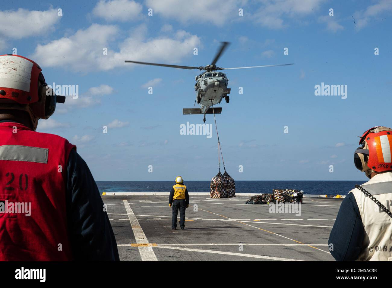 U.S. Navy Sailors observe an MH-60S Sea Hawk landing supplies on to the flight line during a resupply at sea aboard USS Green Bay, Philippine Sea, Feb. 15, 2022. The 31st MEU is operating aboard the ships of the America Amphibious Ready Group in the 7th fleet area of operations to enhance interoperability with allies and partners and serve as a ready response to defend peace and stability in the Indo–Pacific Region. Stock Photo