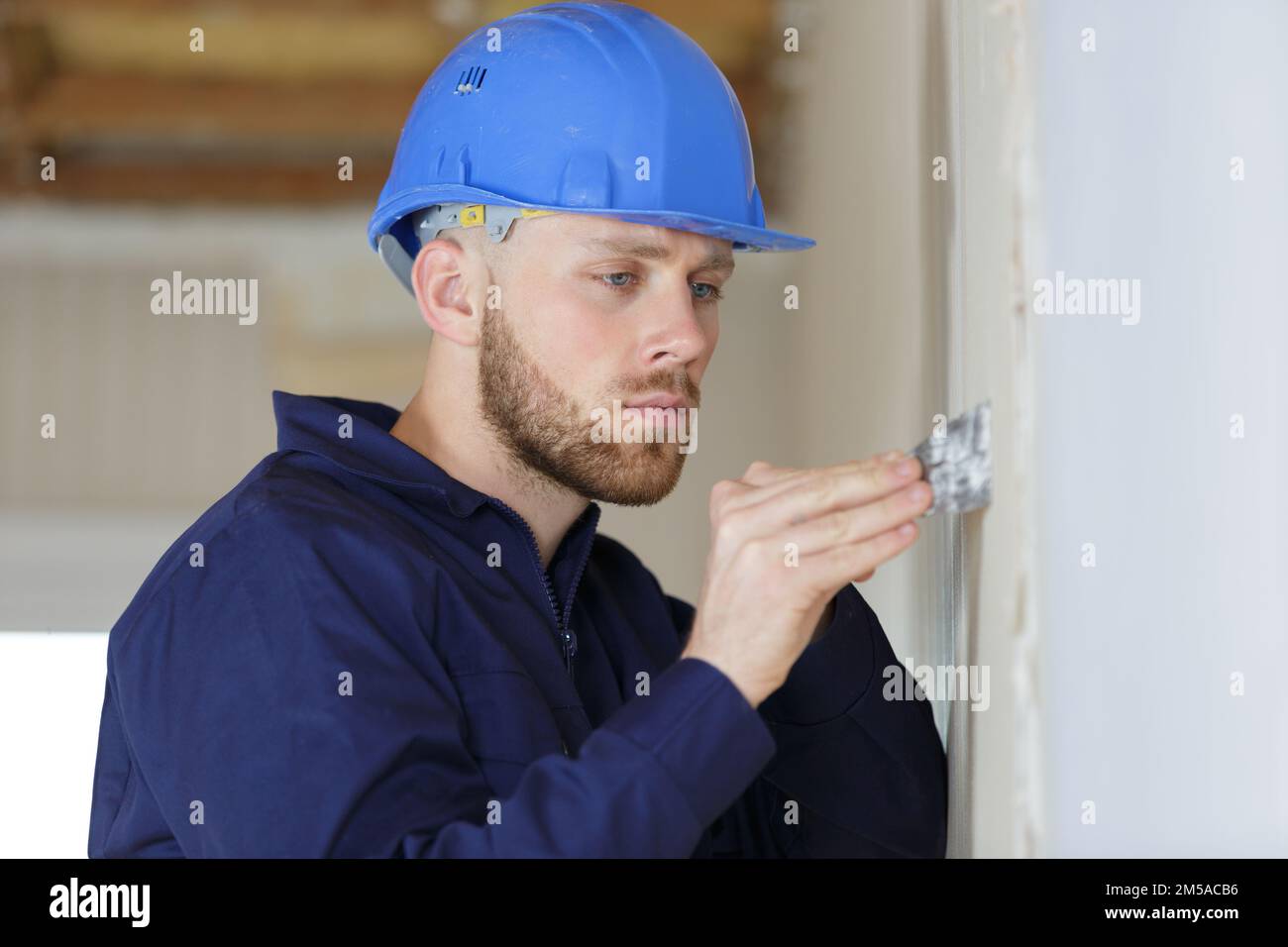 male builder using putty knife on white wall Stock Photo