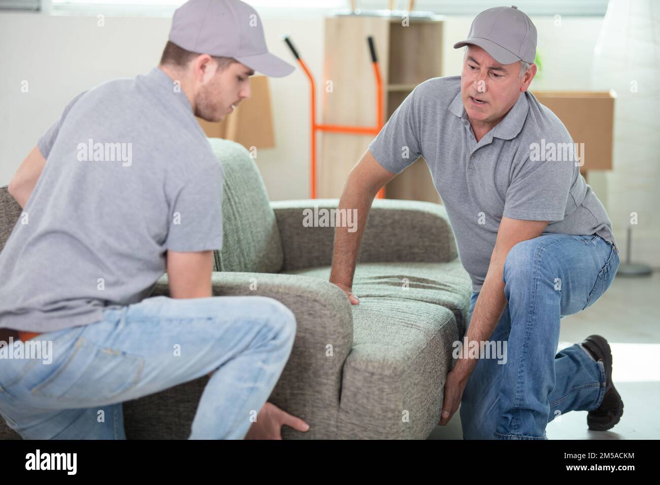 two handsome smiling movers carrying a sofa Stock Photo