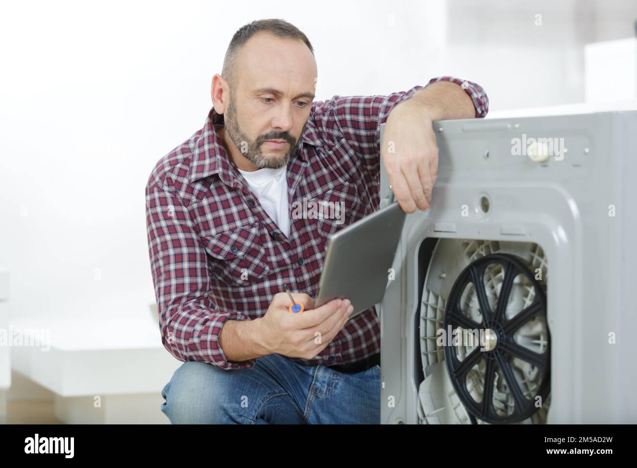 man using tablet to fix a washing machine Stock Photo