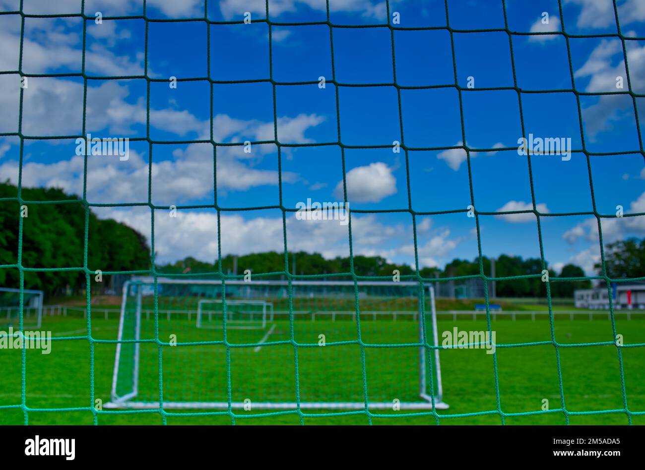 view through a soccer goal net at a deserted sports field with fresh green lawn and a blue sky (variation B) Stock Photo