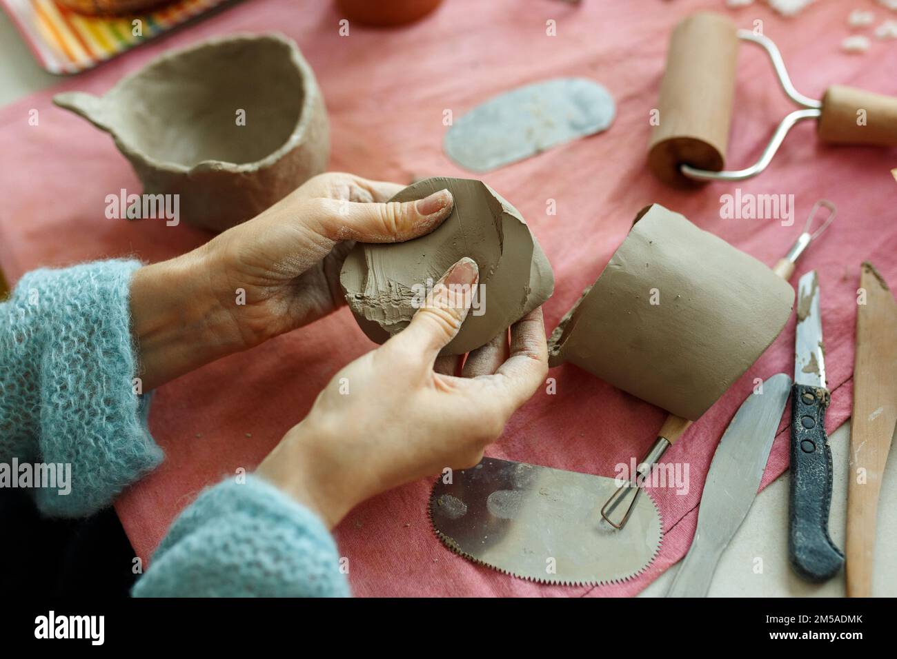 Kneading piece of raw grey clay by female hands on wooden table. DIY
