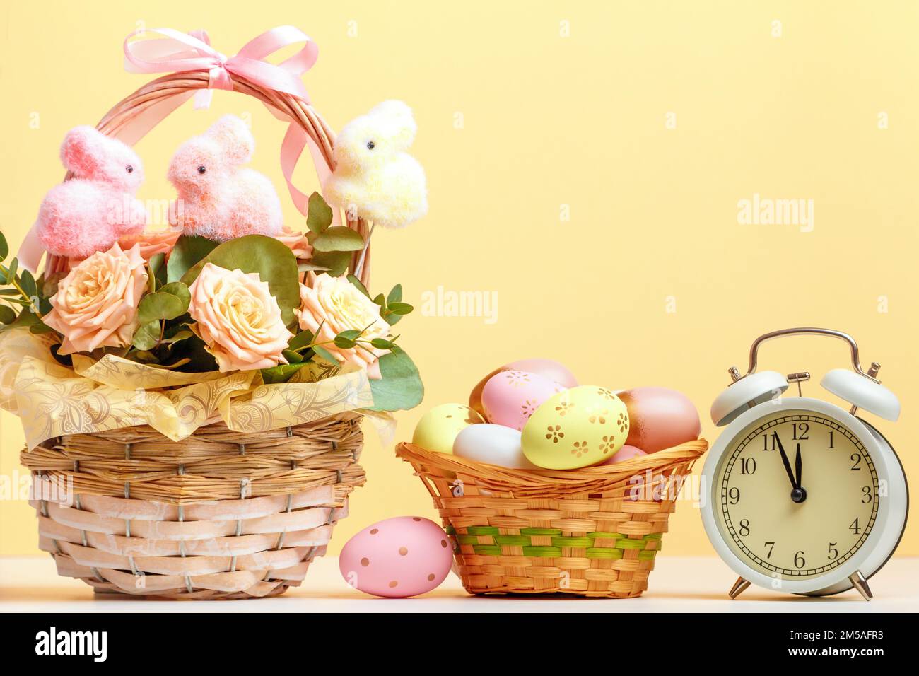 Easter composition still life. Baskets with roses and eggs alarm clock on the table. Stock Photo