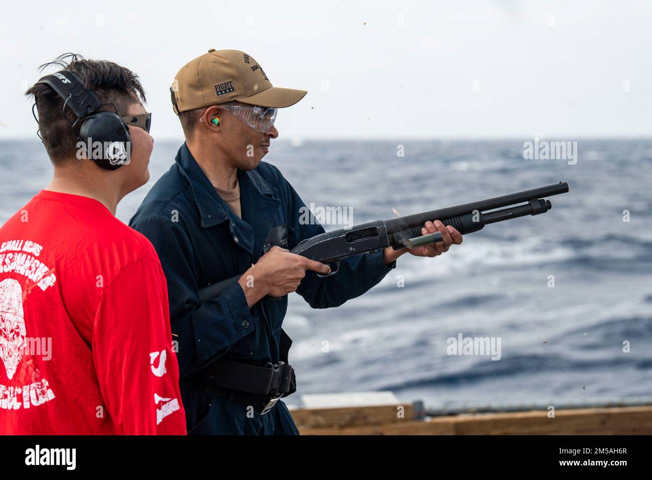 SOUTH CHINA SEA (Feb. 16, 2022) Gunner’s Mate 2nd Class Jeremy Gillentine, left, from Abilene, Texas, acts as Range Safety Officer while Gunner’s Mate Seaman Apprentice Aijai Schultz, from Savannah, Georgia, fires the M500 shotgun during a qualification course aboard the Arleigh Burke-class guided-missile destroyer USS Dewey (DDG 105). Dewey is assigned to Destroyer Squadron (DESRON) 15 and is underway supporting a free and open Indo-Pacific. CTF 71/DESRON 15 is the Navy’s largest forward-deployed DESRON and the U.S. 7th Fleet’s principal surface force. Stock Photo