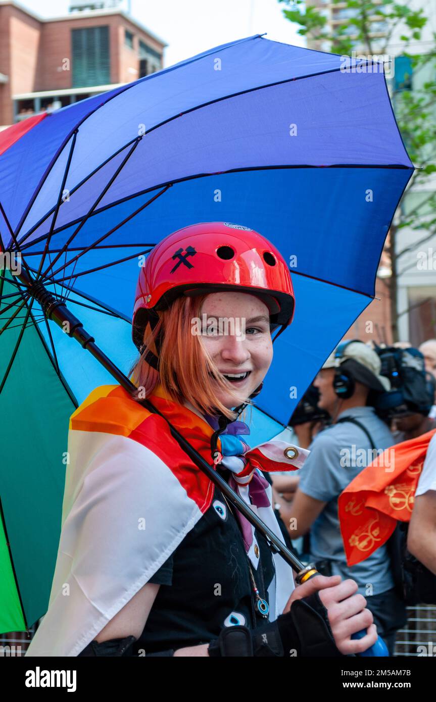 Portrait of a young person skating with a Canadian flag and a rainbow umbrella. She is partaking in the annual celebration of the LGBTQ+ community in Stock Photo
