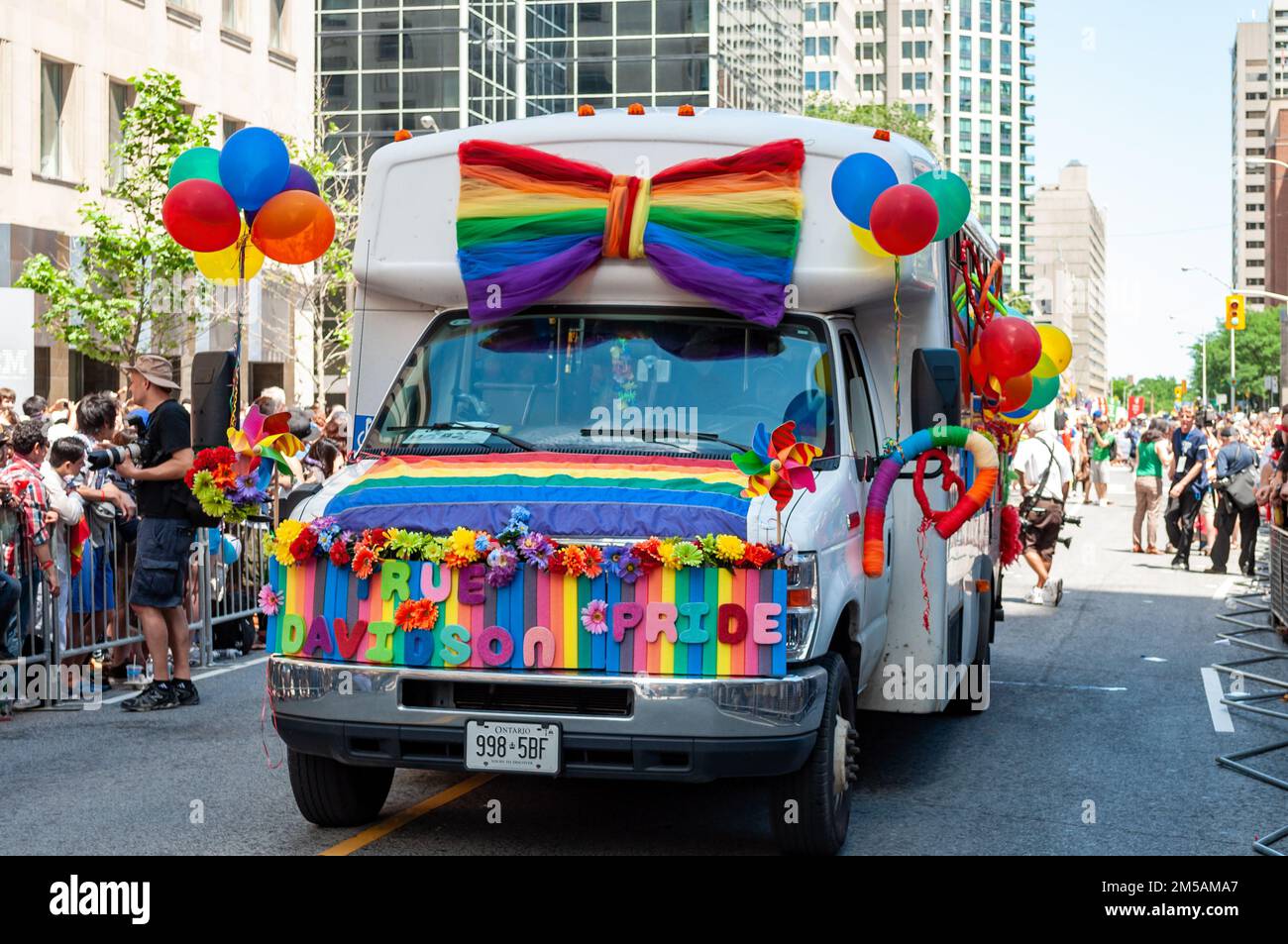 A truck covered with rainbow flags and balloons drives in Bloor Street. The vehicle is part of the annual LGBTQ+ celebration. Stock Photo