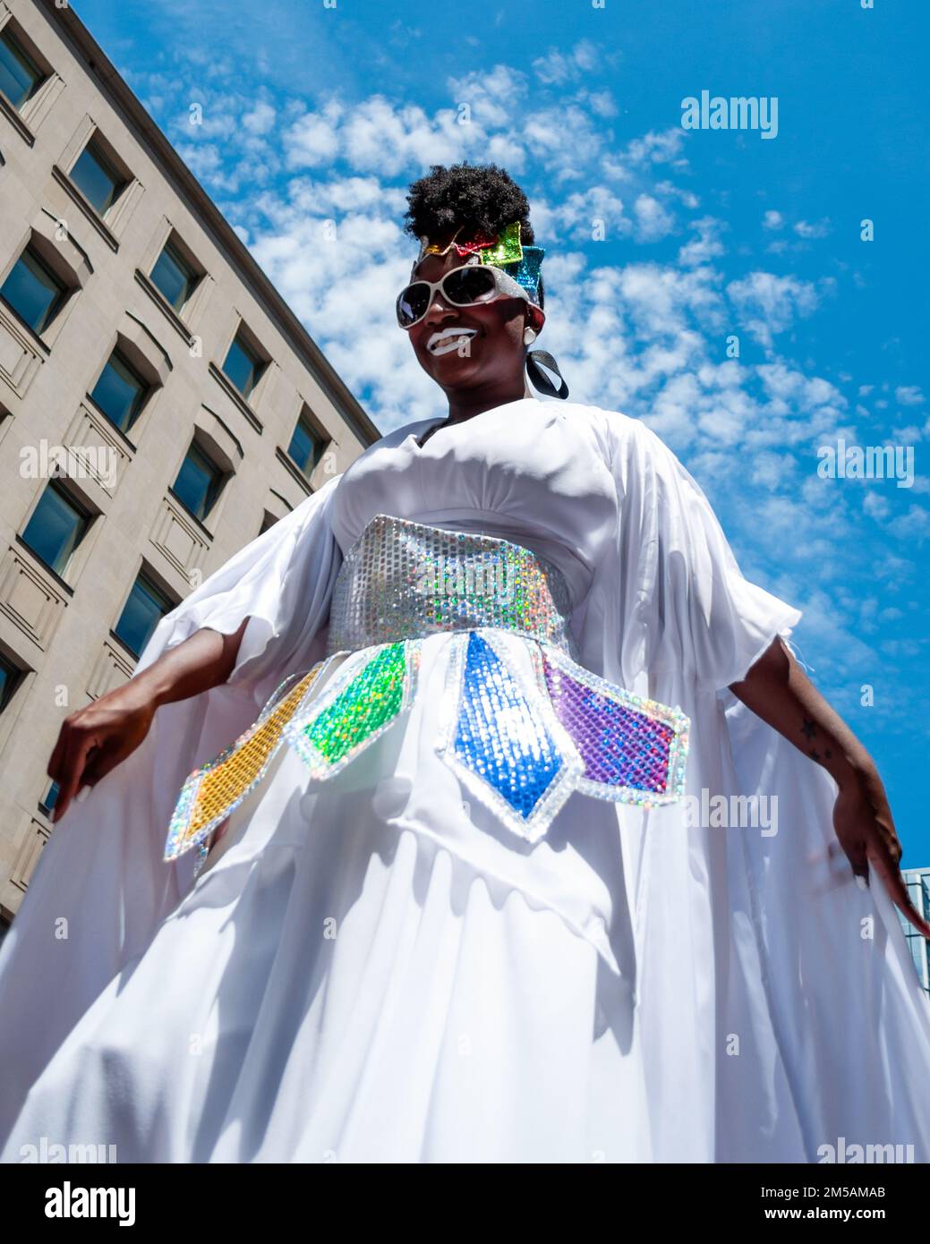 A person of African ethnicity in stilts walks in Bloor St. Low angle view. The event celebrates the LGBTQ community in the city. Stock Photo
