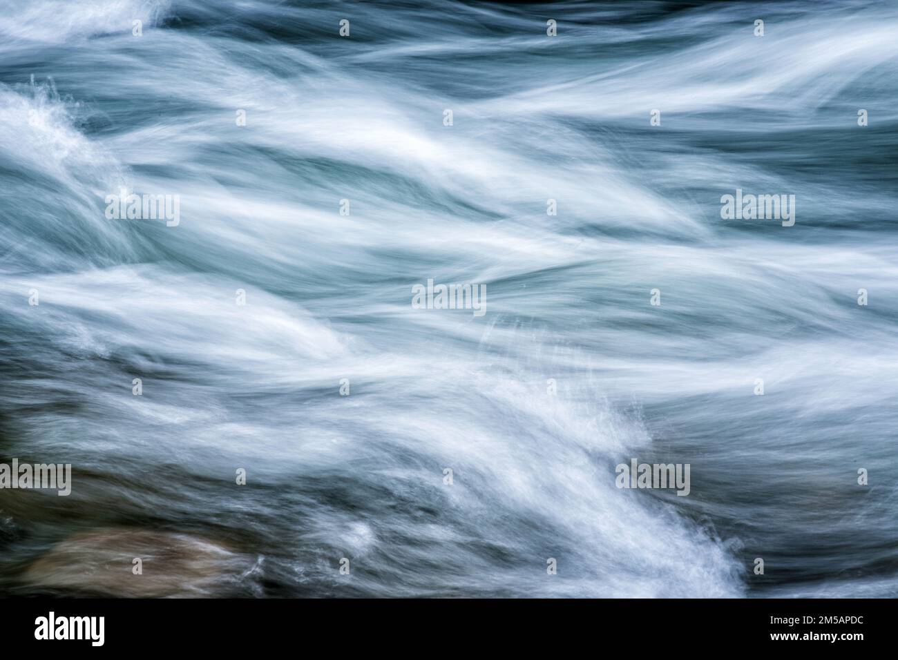 A time exposure of a flowing mountain stream with a large rock at the bottom left. Stock Photo