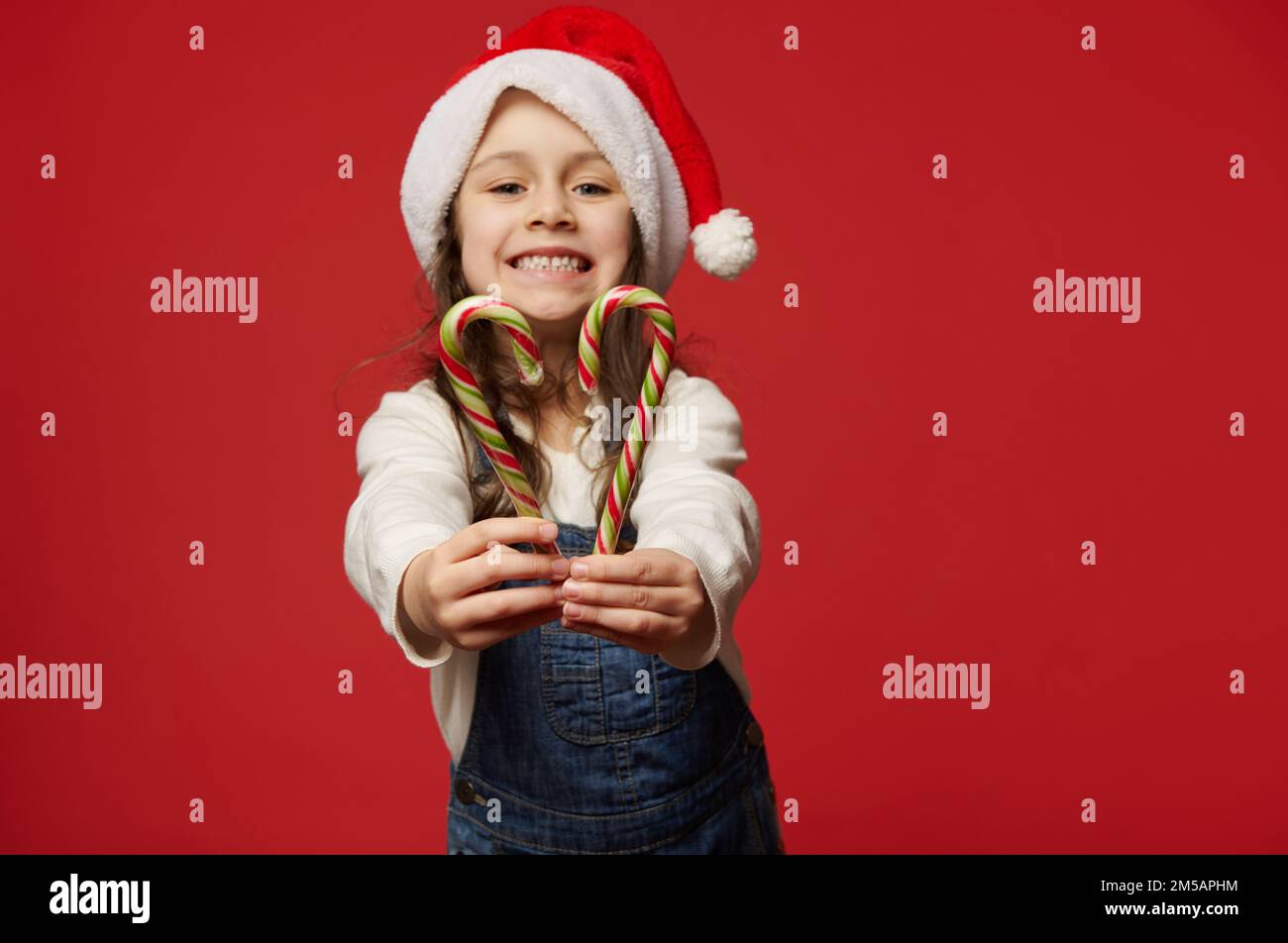 Details hands of child in Santa hat, holding out at camera red green