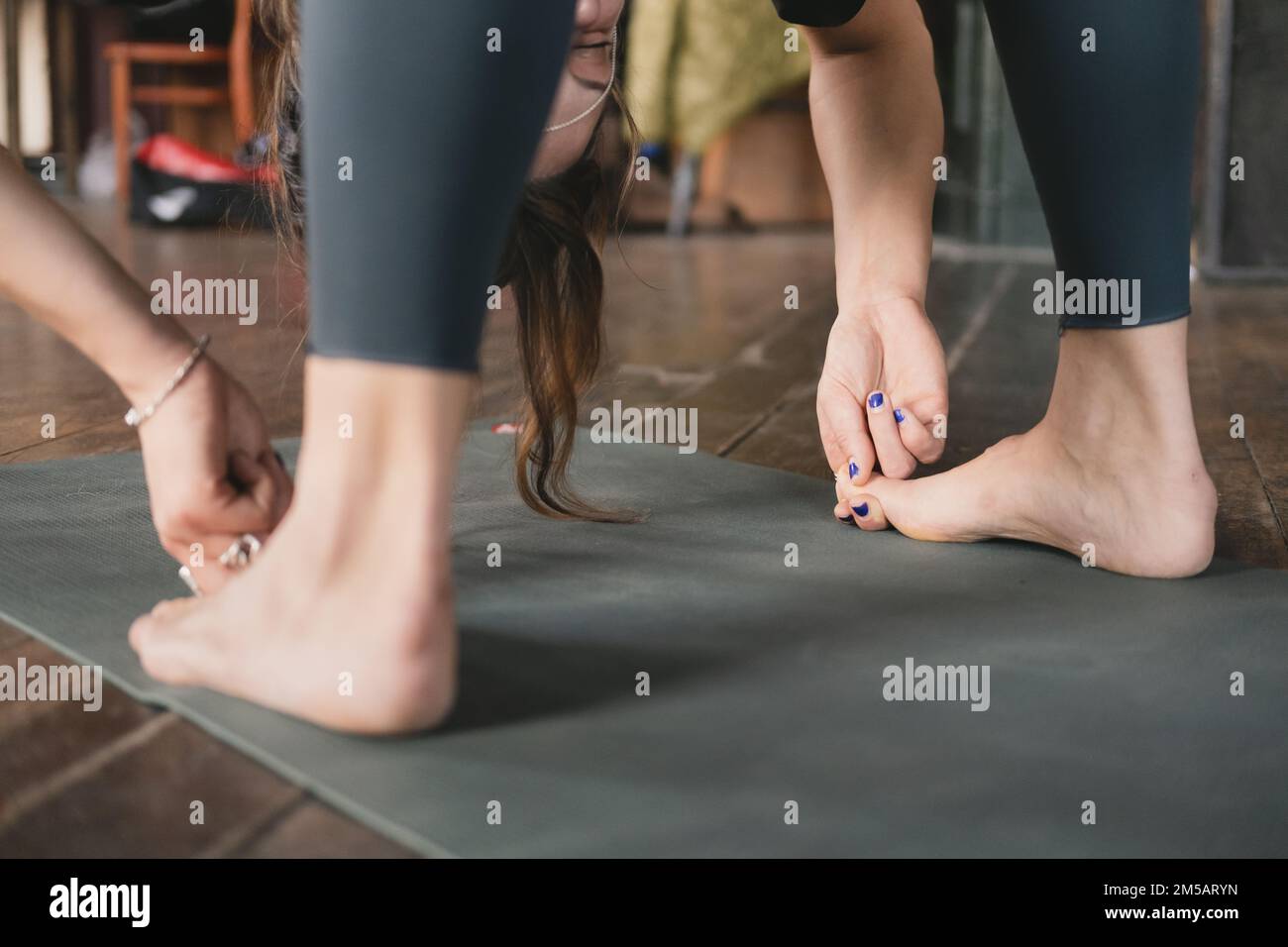 Close-up side photo of a female new yoga teacher doing a standing forward fold pose variation hooking big toes (Padangusthasana) during her vinyasa fl Stock Photo