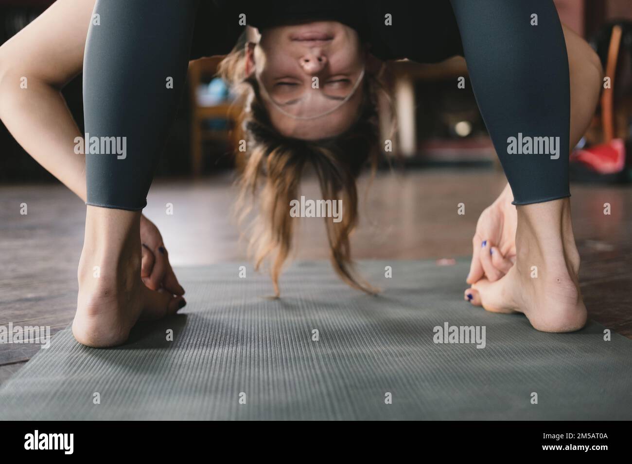 Close-up photo of a female new yoga teacher doing a standing forward fold pose variation hooking big toe during her vinyasa flow yoga practice Stock Photo