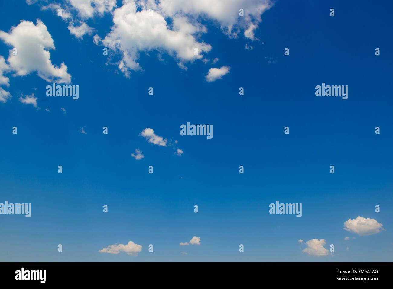 White fluffy clouds and bright sun on dark blue sky. Stock Photo