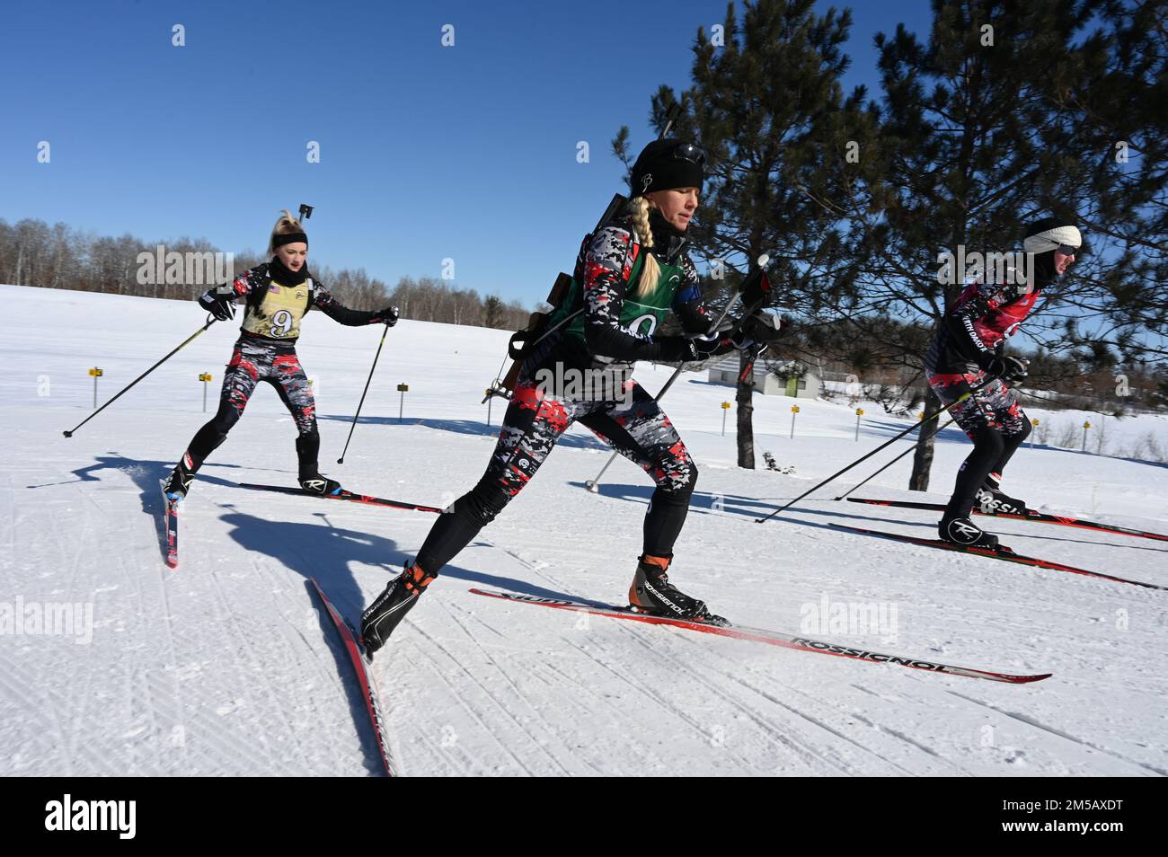 U.S. Army and Air Force members of the North Dakota National Guard from left to right 2nd Lt. Kaitlyn Gura, of the 1,188th Air Defense Artillery Regiment, Senior Master Sgt. Danelle Card, of the 119th Wing, and Spc. Sydney Kautz, of the 188th Engineer Company, cross-country ski away from the shooting range portion of the biathlon patrol race at the Chief of the National Guard Bureau Biathlon Championship held at Camp Ripley, Minn., Feb. 11-17, 2022. The three-member North Dakota team contributed to a second place finish in the women's overall category of the competition with several individual Stock Photo