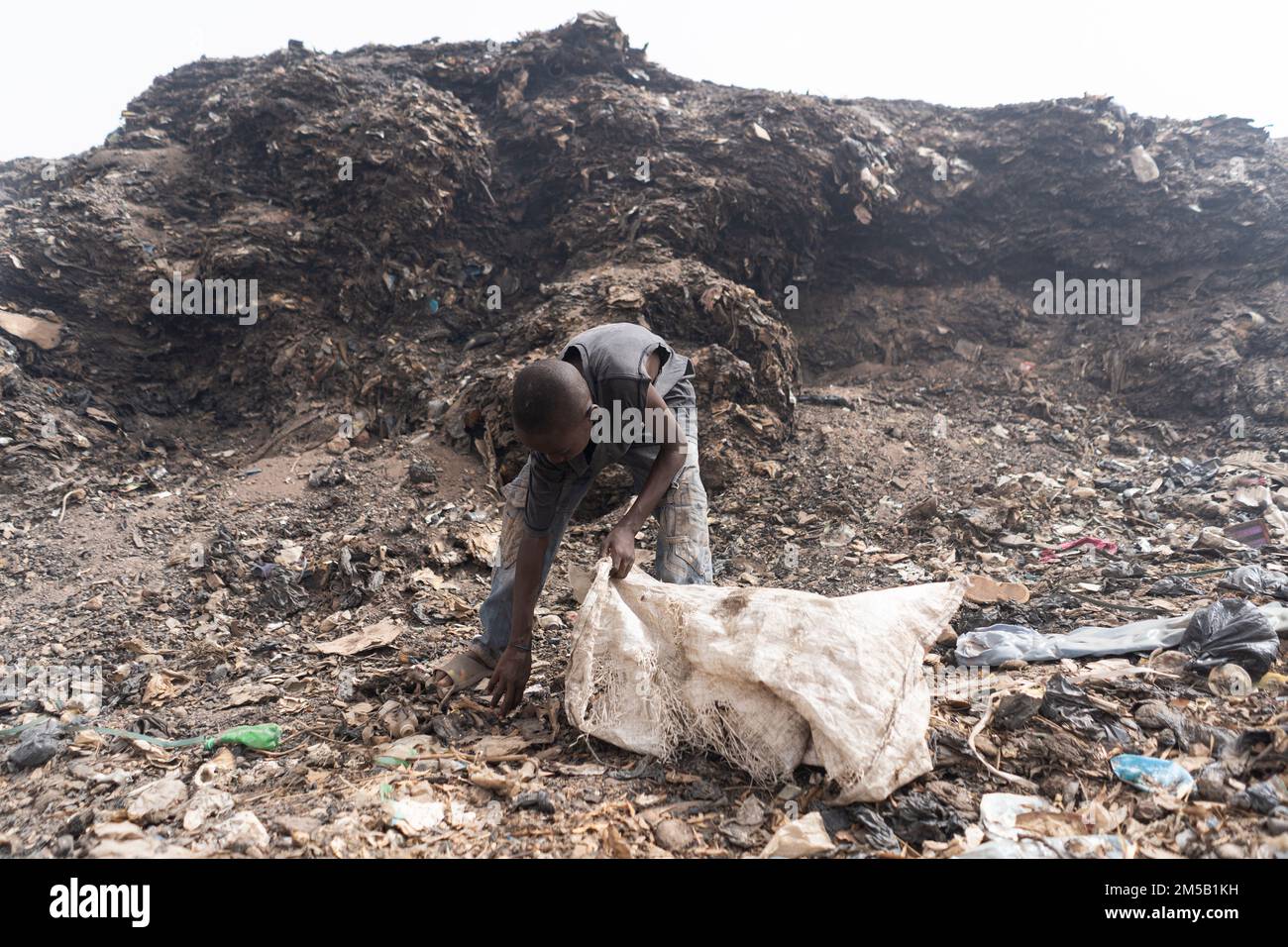 African slum boy collecting reusable items in a garbage dump; symbol of poverty in developing countries Stock Photo