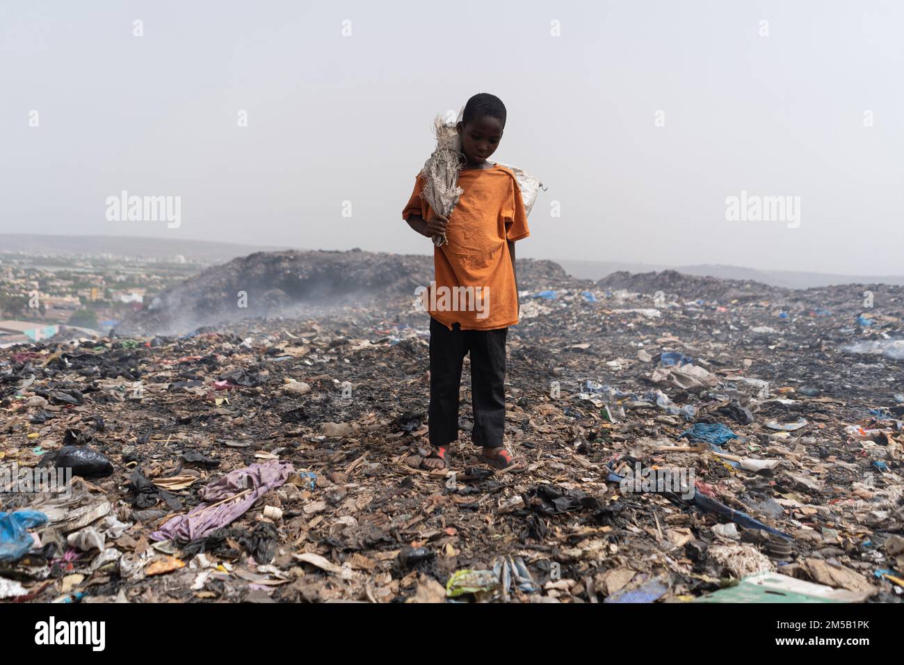 Small African garbage collector scavenging the ground for reusable items Stock Photo