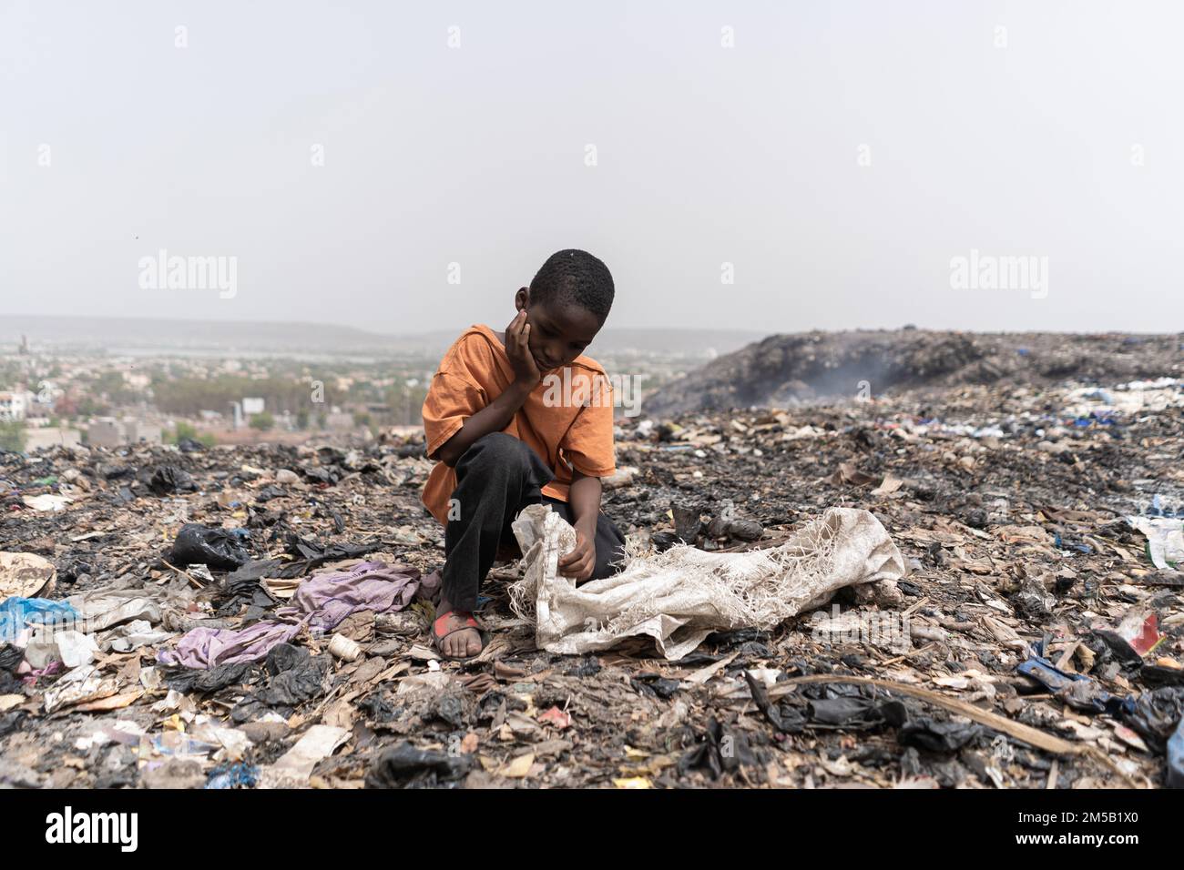 Miserable hungry African slum child looking for edible and recyclable items in a huge urban garbage dump Stock Photo